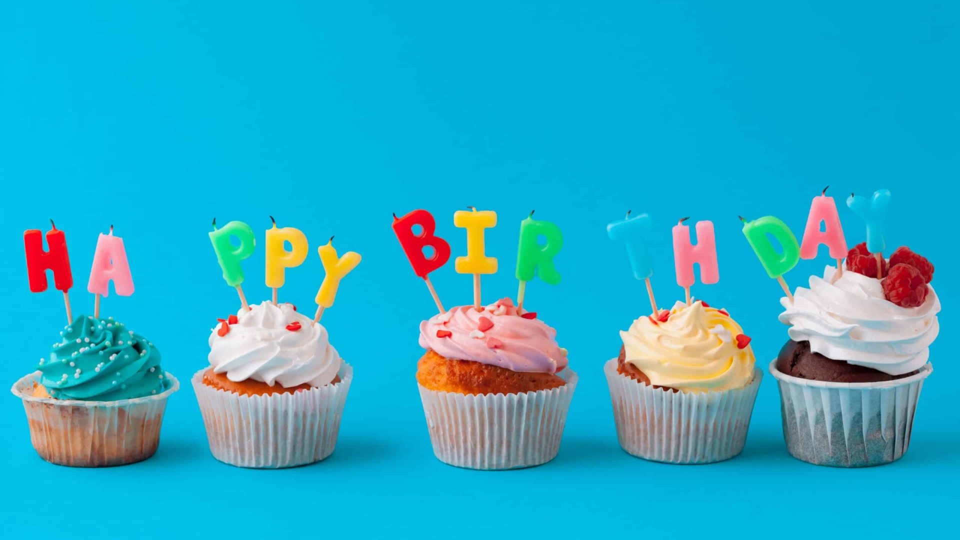 Bunte Cupcakes mit Geburtstagskerzen vor einem farbenfrohen Hintergrund.