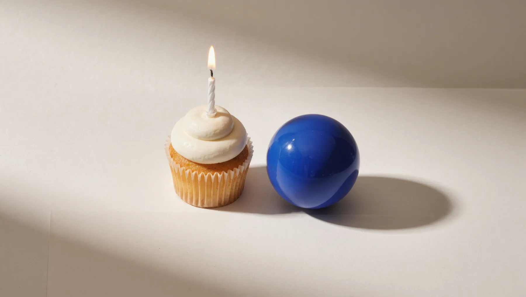 Cupcake mit brennender Kerze neben einer kobaltblauen Kugel