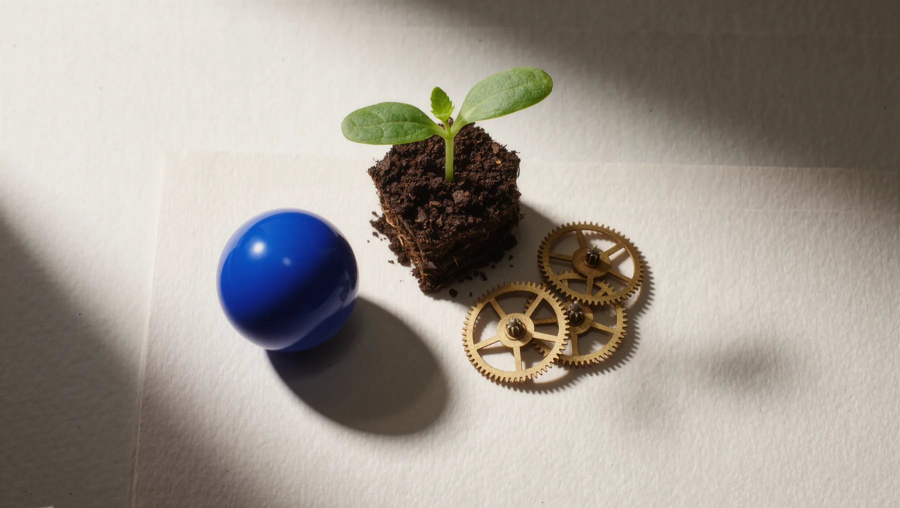 Seedling in soil with small brass gears, a cobalt-blue sphere beside it