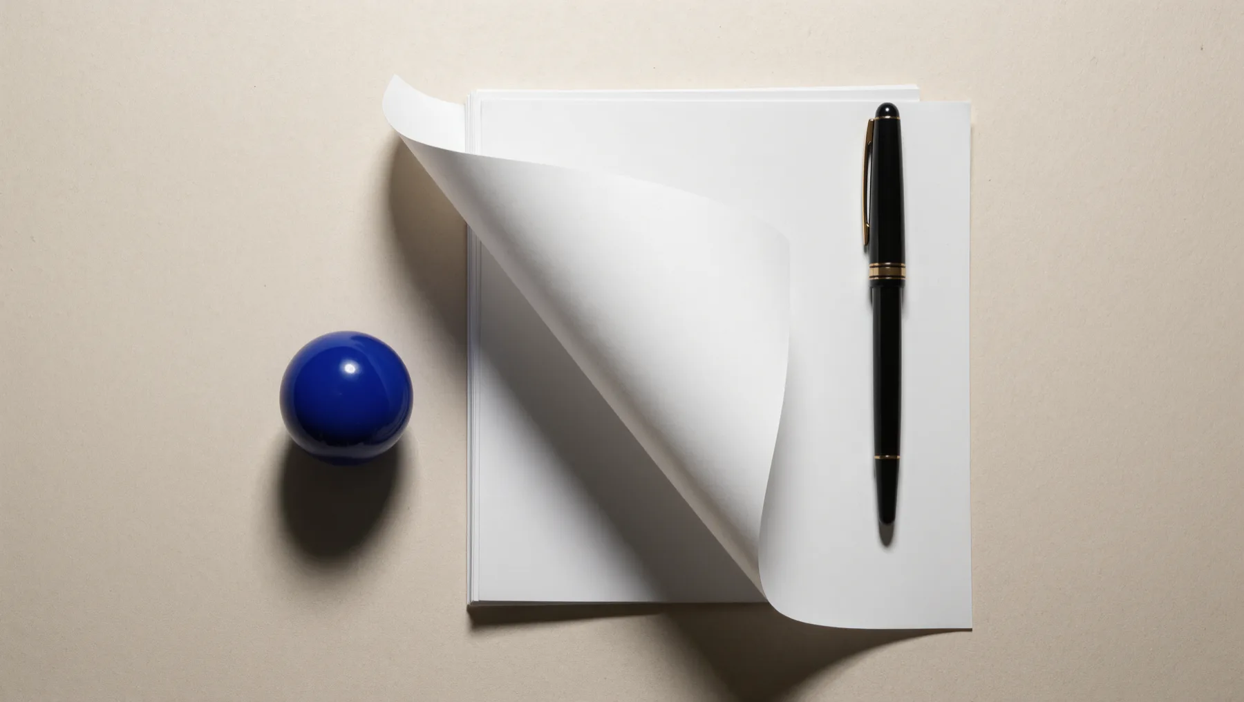 Stack of blank pages with a rolled-up sheet and a fountain pen, a cobalt-blue sphere beside them