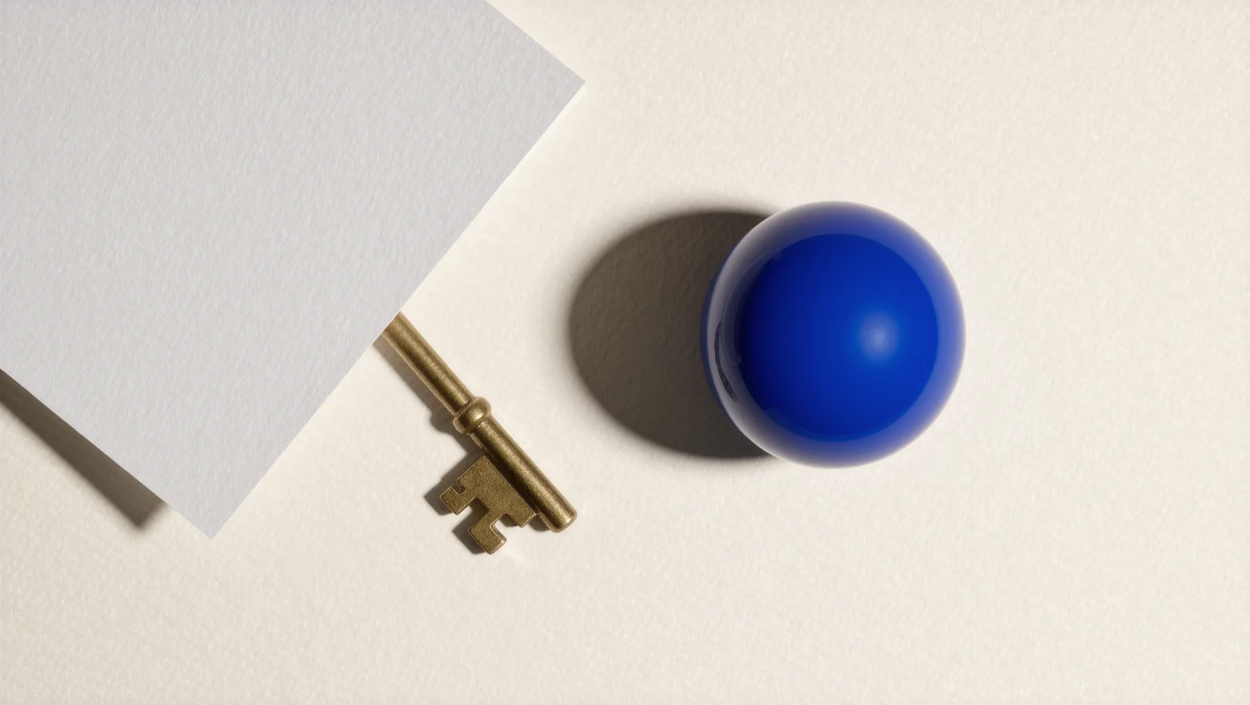 Brass key half hidden under a white card, a cobalt-blue sphere beside it